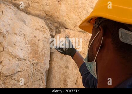 Un agent de préservation injecte un coulis liquide à base de calcaire dans les fissures des pierres vieilles de 2,000 ans du mur de l’Ouest pour les préserver et les renforcer le 23 février 2021, à Jérusalem, en Israël. Les conservateurs de l'Autorité des Antiquités d'Israël ont commencé le travail de conservation pour préparer le mur occidental pour la Pâque. Cette section du mur de soutènement du complexe du Mont du Temple est inspectée et nettoyée deux fois par an, une fois avant la Pâque et l'autre fois avant Rosh Hashanah la nouvelle année juive. Banque D'Images