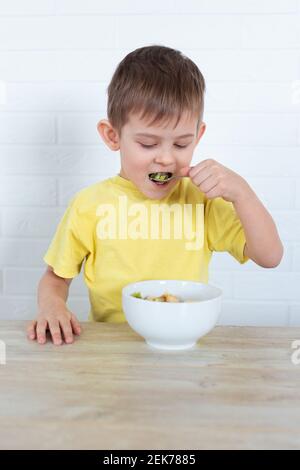 Petit garçon gaucher dans un T-shirt jaune en train de manger de la salade de fruits et sourire. Concept de nourriture saine pour enfants. Produits nutritionnels. Soins de santé. Très bon Banque D'Images