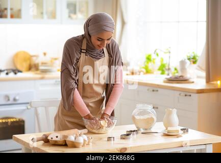 Jeune femme islamique en hijab préparer une pâtisserie dans la cuisine, pétrir la pâte Banque D'Images