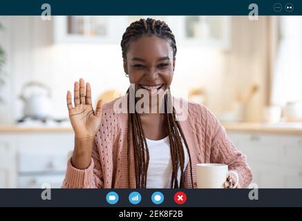 Joyeuse femme noire ayant la vidéo conférence tout en buvant le café dans la cuisine, Capture d'écran Banque D'Images