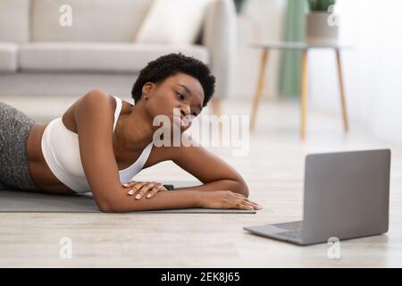 Femme africaine couchée près d'un ordinateur portable fatiguée après un entraînement en ligne en intérieur Banque D'Images