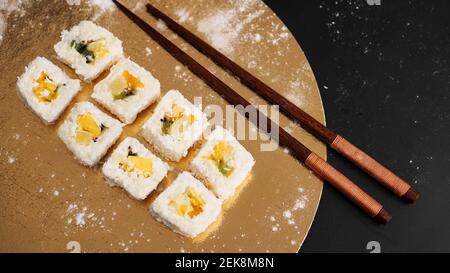 Livraison de sushis. Petits pains sucrés à base de riz, ananas, kiwi et mangue. Roule sur un fond doré et noir. Bâtonnets en bois pour sushi. Banque D'Images