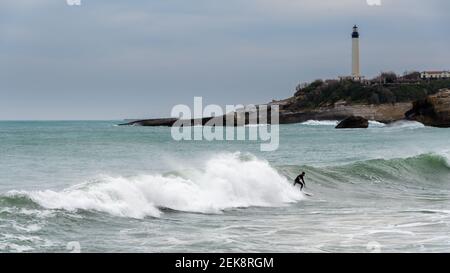 Un surfeur surfant sur une vague à Biarritz, France. Le phare de Biarritz est visible en arrière-plan. Ciel nuageux d'hiver Banque D'Images