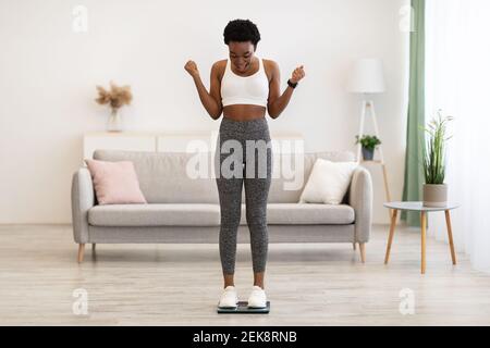 Une femme africaine excitée sur les balances de poids secouant les poings après avoir fait des amincissants à l'intérieur Banque D'Images