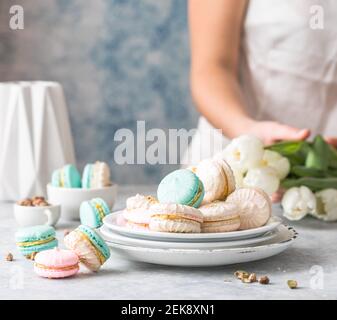 Des macarons français ou italiens colorés s'empilent sur une assiette rouge. Dessert pour le thé de l'après-midi ou la pause café. Magnifique cadre repas avec femme Banque D'Images