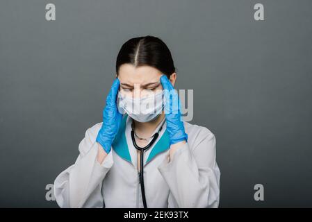 Belle femme médecin dans le masque protecteur regardant loin et pensant à quelque chose. Banque D'Images