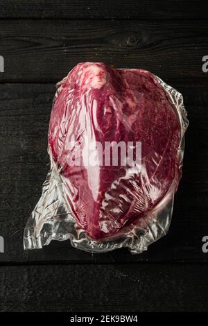 Viande de bœuf ronde dans un set sous vide, sur fond de table en bois noir, plan de dessus Banque D'Images