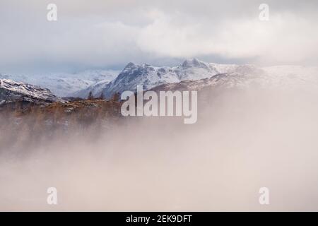 Chaîne de montagnes enneigée dans un paysage hivernal majestueux et brumeux. Langdale Pikes, Lake District, Angleterre. Banque D'Images