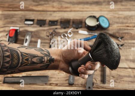 Main de coiffeur avec équipement sur fond de table en bois. Gros plan ciseaux, peigne, brosses, rasoirs, outils professionnels de coiffeur. Métier professionnel, art, concept d'auto-soins. Magazine. Banque D'Images