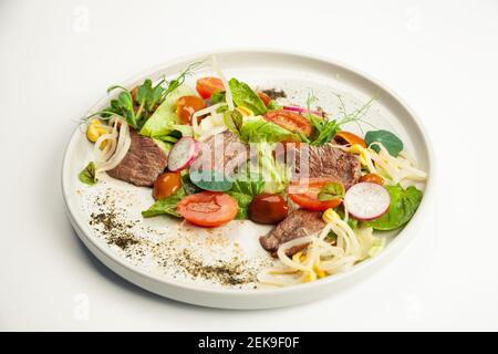 Salade avec tatatataki de bœuf sur une assiette. Ingrédients laitue Iceberg, bœuf tatataki, champignons nameko, tomates cerises, moashi, épinards, sauce ponzu. Pour le menu du restaurant. Banque D'Images