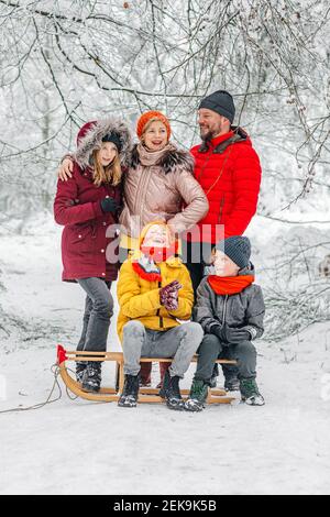 Parents debout par des enfants assis en traîneau dans la forêt pendant hiver Banque D'Images