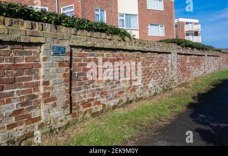 Un vieux mur de briques rouges, décoloré, abîmé et usé le long d'une allée à West Sussex, Angleterre, Royaume-Uni. Banque D'Images