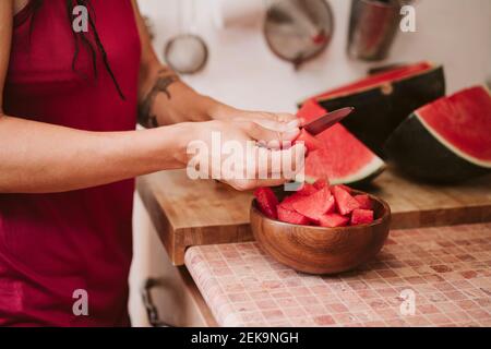 La pastèque coupe femme debout dans la cuisine à la maison Banque D'Images