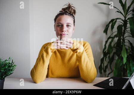 Femme confiante avec la main sur le menton en regardant tout en étant assis près table à la maison Banque D'Images
