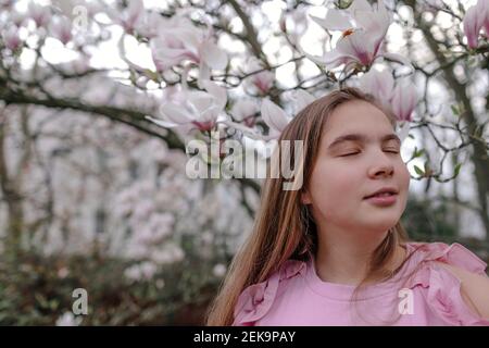 Adolescente avec les yeux fermés contre le magnolia dans le parc Banque D'Images
