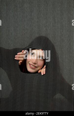 Portrait de la jeune femme souriant à travers le trou en rayures grises arrière-plan Banque D'Images