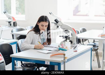 Jeune chercheur en manteau blanc prenant des notes en classe scientifique Banque D'Images