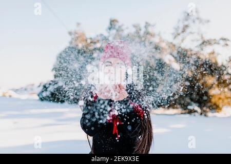 Femme ludique qui soufflait de neige tout en profitant de vacances à la campagne Banque D'Images