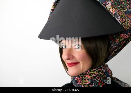 Femme souriante portant un abat-jour noir avec foulard sur blanc mur Banque D'Images