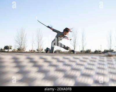 Jeune femme à l'épée pratiquant les arts martiaux dans le parc contre ciel dégagé Banque D'Images