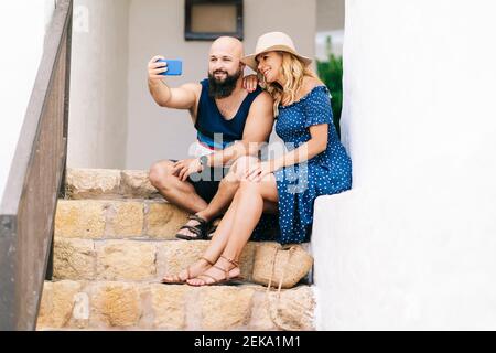 Des amis qui prennent leur selfie avec leur smartphone tout en étant assis sur des marches au village de Binibeca, Minorque, Espagne Banque D'Images