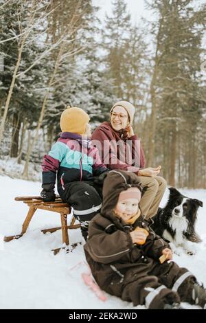 Mère souriante avec sa fille assise tout en passant un week-end en famille Et Border Collie en hiver dans la neige Banque D'Images