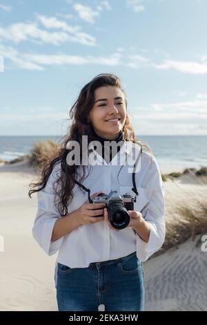 Jeune femme souriante avec un appareil photo à la plage Banque D'Images