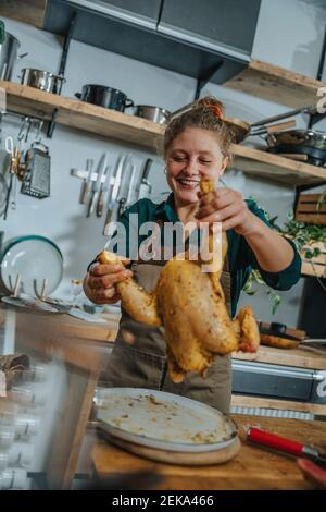Jeune chef souriant tout en marinant de la viande de poulet debout dans la cuisine Banque D'Images