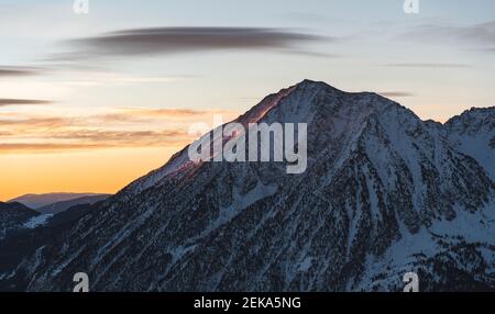 Montagne rocheuse couverte de neige dans un ciel nuageux au coucher du soleil Banque D'Images