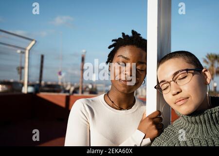 Amis femelles avec les yeux fermés penchée sur le poteau Banque D'Images