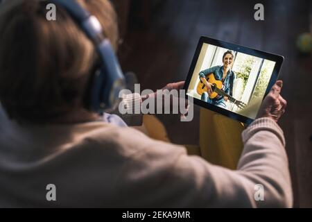 Jeune femme jouant de la guitare pour femme senior sur appel vidéo via une tablette numérique à la maison Banque D'Images