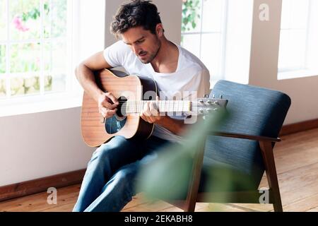 Homme pratiquant à la guitare assis sur un fauteuil à la maison Banque D'Images