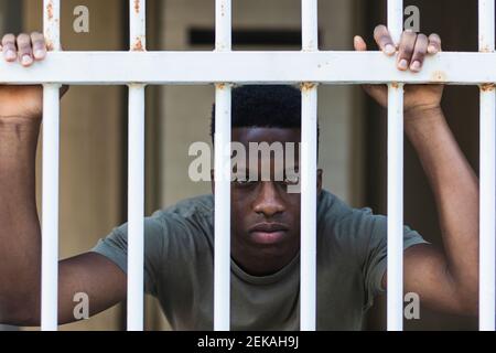 Jeune homme regardant à travers la clôture métallique rouillée Banque D'Images