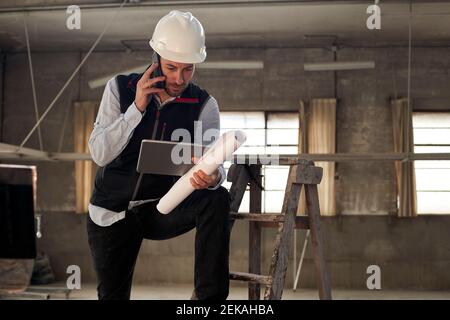 Un ingénieur parlant sur un téléphone portable tout en utilisant une tablette numérique dans le bâtiment Banque D'Images