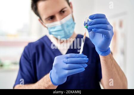 Médecin avec masque facial de protection, seringue de remplissage avec le vaccin COVID-19 Banque D'Images