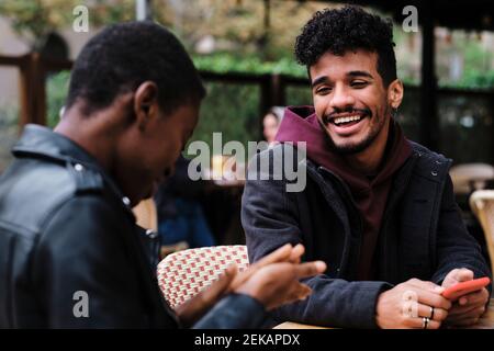 Homme souriant regardant un ami assis au café-terrasse Banque D'Images