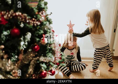 Fille ludique assise à pattes croisées avec la famille par arbre de Noël à la maison Banque D'Images