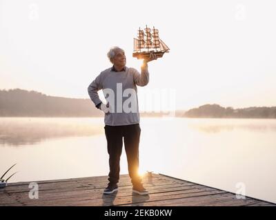 Homme tenant un voilier debout avec la main sur la hanche contre le lac Banque D'Images