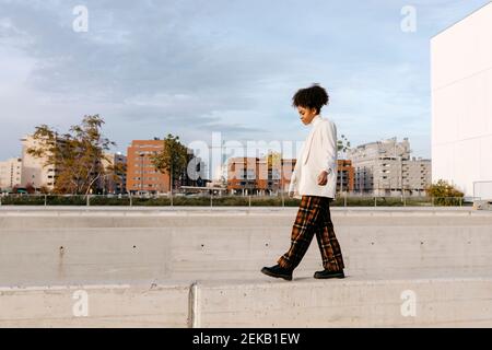 Jeune femme avec cheveux afro marchant sur le mur de retenue contre les bâtiments de la ville Banque D'Images