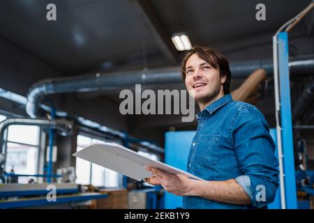 Inspecteur masculin avec dossier souriant tout en se tenant à l'industrie Banque D'Images