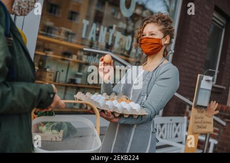 Femme commis dans le masque vendant des œufs au client à l'organique Magasin de détail pendant la période COVID-19 Banque D'Images