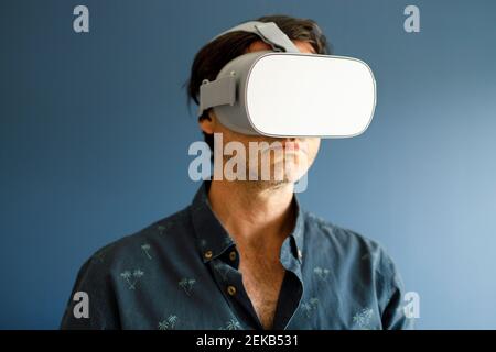 Homme regardant un film à travers le simulateur de réalité virtuelle tout en faisant des gestes contre le mur bleu Banque D'Images