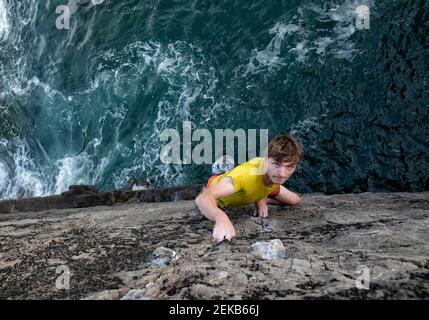 Jeune homme passionné grimpeur de rocher grimpant la falaise rocheuse par mer Banque D'Images