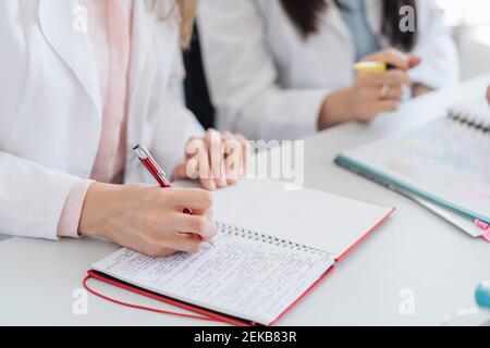 Rogner la vue des mains de l'étudiant prenant des notes dans le bloc-notes en cours de sciences Banque D'Images