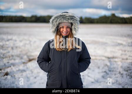 Belle femme souriante avec les mains dans les poches debout sur la neige champ contre ciel Banque D'Images