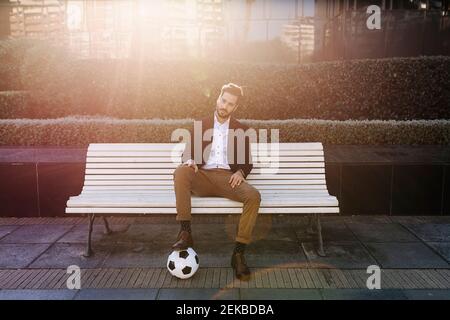 Homme d'affaires adulte de taille moyenne avec un ballon de football assis sur un banc Banque D'Images