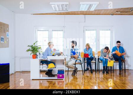 Vue latérale des personnes assises en ligne avec des dossiers dans les mains et attendant un entretien d'emploi. Banque D'Images