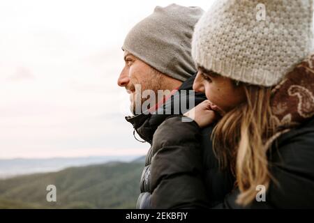 Couple souriant dans des vêtements chauds regardant loin pendant l'hiver Banque D'Images