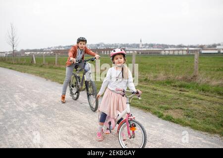Frère et sœur avec des vélos sur la route contre le ciel clair Banque D'Images