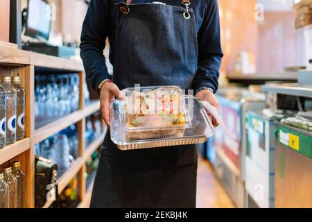 Gestionnaire mâle mature tenant des récipients en feuille et en plastique pendant le travail dans le restaurant Banque D'Images